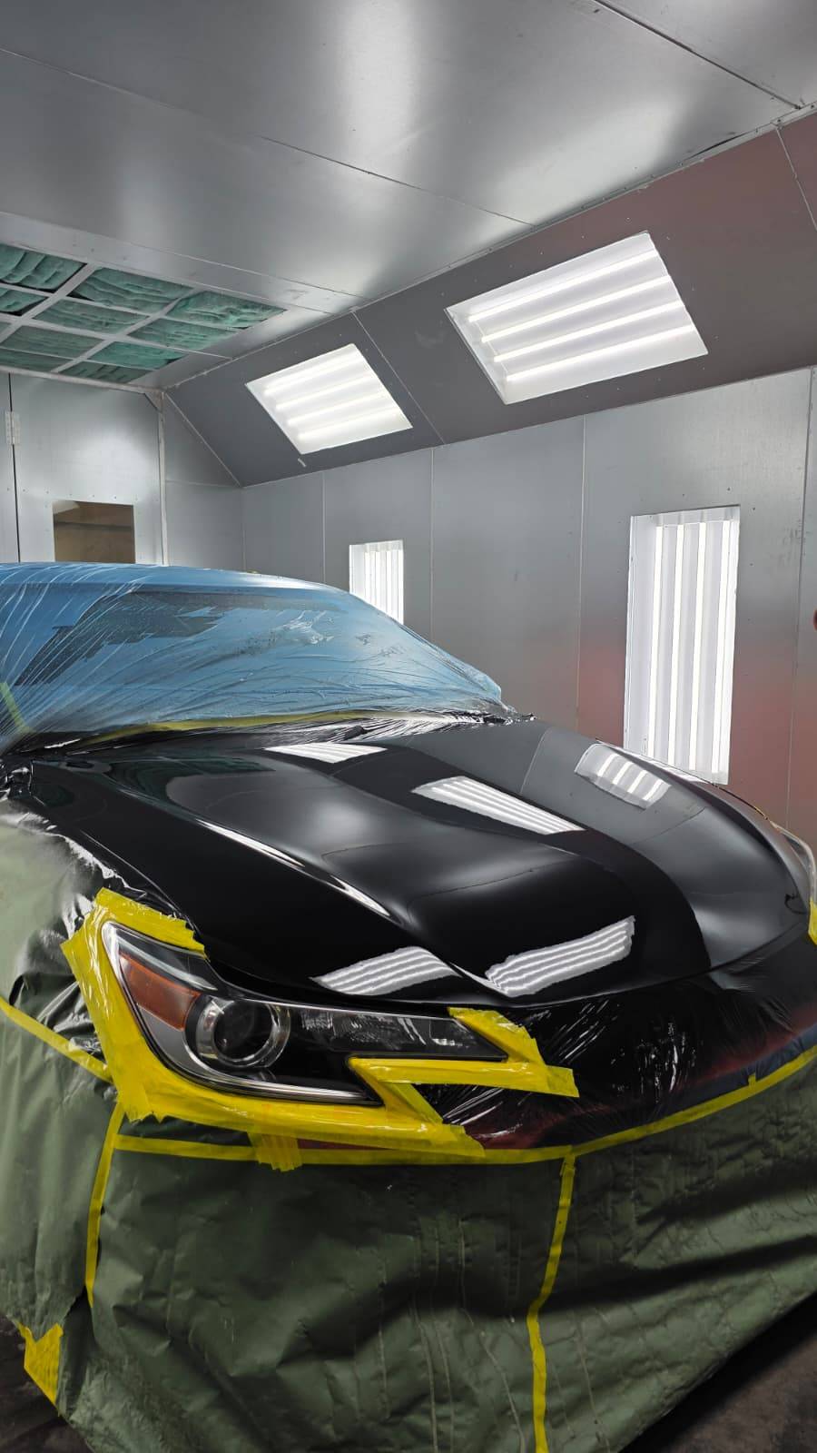 Black car masked with yellow tape in paint booth